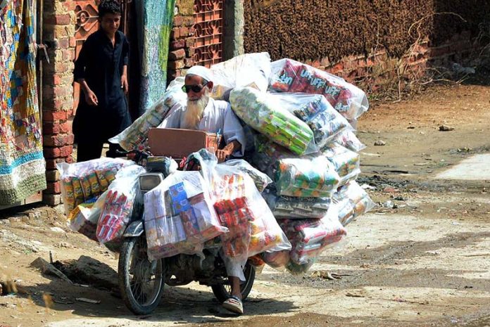 A view of daily toil as an elderly motorcyclist balances a stack of chips and snake packets on his motorcycle during a delivery in Latifabad