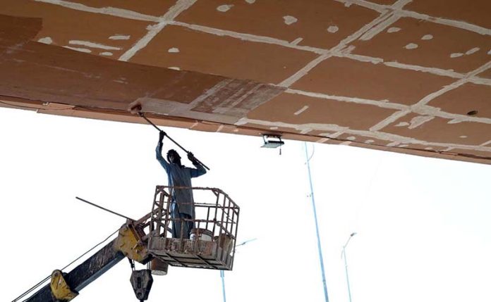 Worker is busy paint the bridge at Peshawar Mor Interchange in the Federal Capital