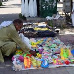A vendor arranging and displaying children’s plastic toys on the footpath to attract customers in the Federal Capital