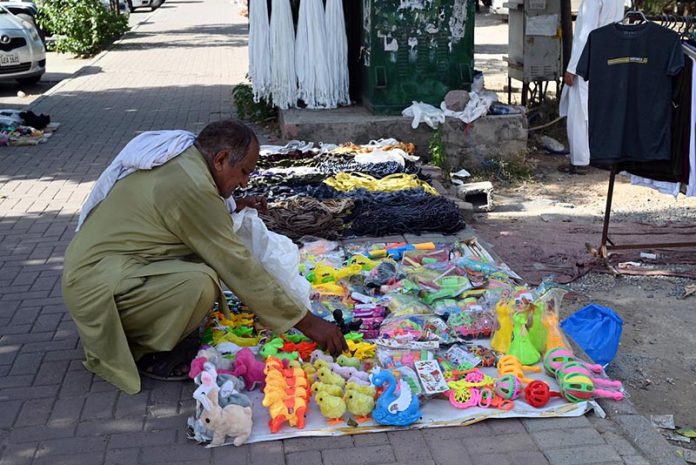 A vendor arranging and displaying children’s plastic toys on the footpath to attract customers in the Federal Capital
