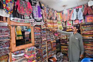 A vendor arranging and displaying traditional Balochi dresses to attract the customer at his shop in a local market.