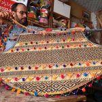 A craftsman is giving the final touches to a handmade decorative fan at his workplace