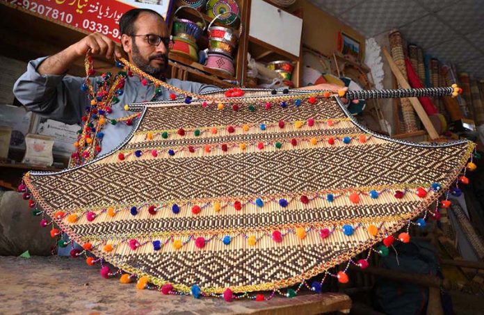 A craftsman is giving the final touches to a handmade decorative fan at his workplace