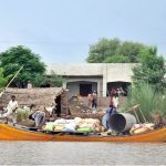 Flood-affected villagers navigate a boat through submerged areas near their homes, transporting relief goods and their belongings