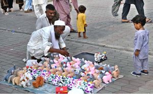 A child looks on anxiously as a vendor arranges and displays toys in Sunday Bazaar at Peshawar Morr.