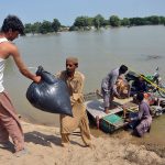 Flood-affected people transporting their belongings on a makeshift raft after their homes were submerged, as locals use self-made boats to evacuate from inundated areas following deadly flash floods in various parts of Punjab.