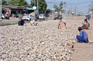 Laborers break and spread stones during road construction work on Vehari Road as development projects continue in the city.
