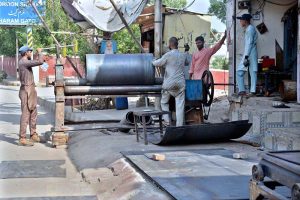 Workers are busy folding large metal sheets on a rolling machine