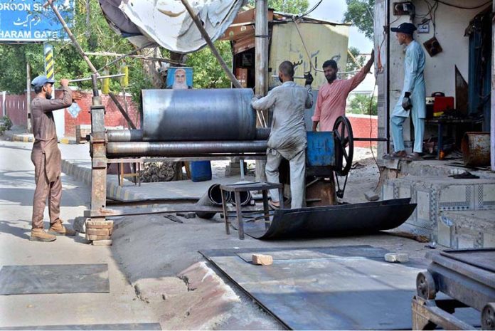Workers are busy folding large metal sheets on a rolling machine