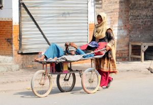 A woman pushes a wheelchair carrying a disabled person while seeking alms on the roadside.