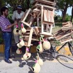 A vendor displaying and selling wooden benches and handmade nests on his bicycle to attract customers along a roadside in the Federal Capital