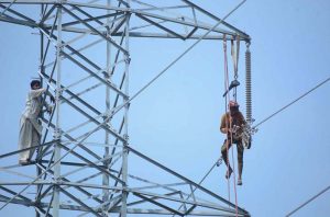 WAPDA workers carry out repair and maintenance on a high-voltage transmission line without safety gear, posing the risk of mishaps, as they strive to ensure uninterrupted power supply.