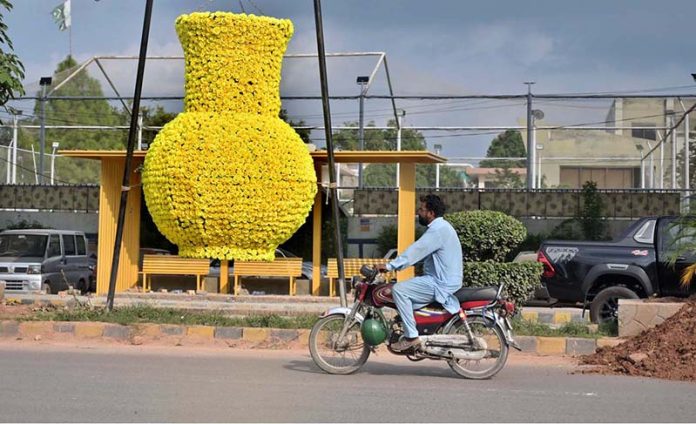 A huge pot, decorated with artificial flowers for city beautification, is displayed along Murree Road