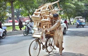 A street vendor pushes his bicycle loaded with handmade wooden stools, hoping to attract buyers on a hot afternoon in the city.