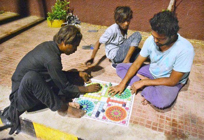 People enjoying a game of ludo while sitting on the footpath outside Radio Pakistan Road