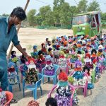 A roadside vendor neatly arranges colorful handmade dolls in the rows on plastic chairs to attract buyers along a busy road.