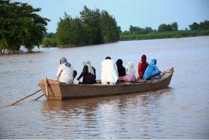 A flood-affected family being rescued by boat to cross floodwaters and move to a safer place in Bhuwana Tehsil near the Chenab River
