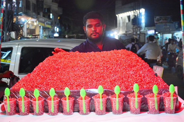 A vendor displays freshly served red pomegranate seeds in disposable glasses with spoons on his handcart to attract customers at Gul Center