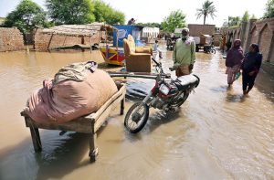 Flood-affected villagers wait for rescuers outside their flooded homes to move families and belongings from flood hit area.