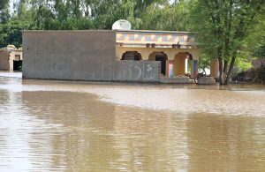 Flood-affected villagers wait for rescuers outside their flooded homes to move families and belongings from flood hit area.