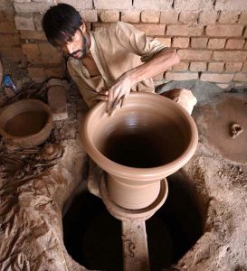 A porter skillfully molding traditional clay pots at his work place in Phandu area.