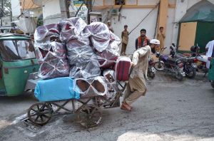 Laborer struggling to push handcart loaded with suitcases at Kohati Chowk.
