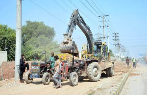 Workers loading mud with the help of a machine on tractor trolly after digging during the construction work of old Shujabad Link Road.