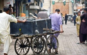 Workers push a cart loaded with water tanks to shift for sale in the market as the city facing water crisis.