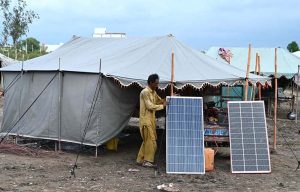 A man installs solar panels to generate electricity from sunlight in front of his makeshift tent near Qambar Bypass Road.