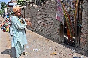 A snake charmer plays the flute to attract children while strolling through a street in Gharibabad Colony.