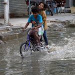 Kids cycle through accumulated rainwater on a street in Gulshan-e-Kaneez Fatima Society, where flooded roads continue to cause severe problems for residents despite the rain having stopped for two days