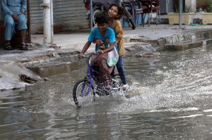 Kids cycle through accumulated rainwater on a street in Gulshan-e-Kaneez Fatima Society, where flooded roads continue to cause severe problems for residents despite the rain having stopped for two days