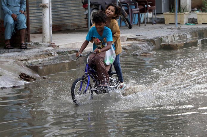 Kids cycle through accumulated rainwater on a street in Gulshan-e-Kaneez Fatima Society, where flooded roads continue to cause severe problems for residents despite the rain having stopped for two days