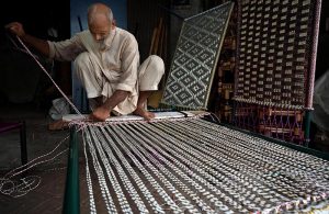 An elderly labourer busy knitting a traditional bed (charpai) for customers outside his shop at a local market in the provincial capital.