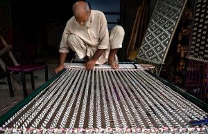 An elderly labourer busy knitting a traditional bed (charpai) for customers outside his shop at a local market in the provincial capital.