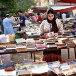A woman selects and buys old books from a stall at Mall Road.