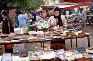 A woman selects and buys old books from a stall at Mall Road.