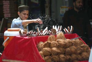 A young street vendor sprinkles water on coconuts to keep them fresh on his hand cart to attract passerby for selling on Saddar Road.