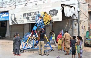 Children enjoy a ride on a portable mini sky wheel swing after paying to swings seller in Jinnah Colony