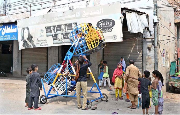Children enjoy a ride on a portable mini sky wheel swing after paying to swings seller in Jinnah Colony