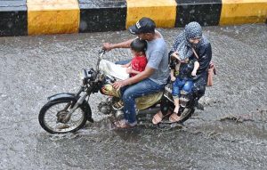A family rides a motorcycle through accumulated rainwater during a rain shower in the city.