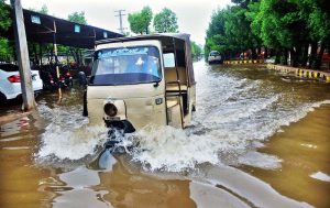A rickshaw passes through rainwater accumulated near Shehbaz Building after heavy rain.