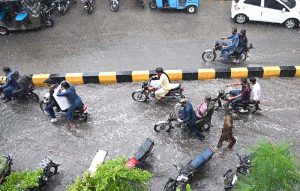 A family rides a motorcycle through accumulated rainwater during a rain shower in the city.