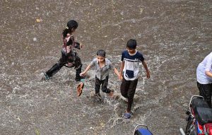 A couple rides a motorcycle through accumulated rainwater during a rain shower in the city.