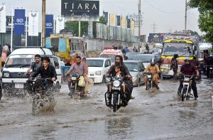 A family rides a motorcycle through accumulated rainwater during a rain shower in the city.