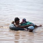 Flood-affected villagers use a tyre tube as a lifesaver to wade through floodwaters in search of shelter