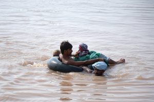 Flood-affected villagers use a tyre tube as a lifesaver to wade through floodwaters in search of shelter