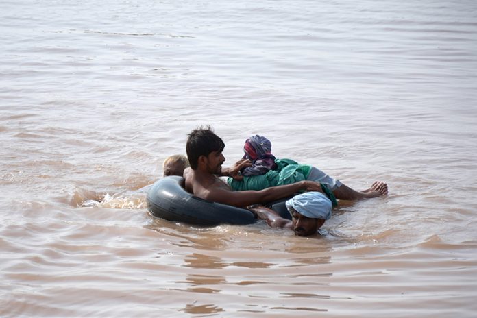 Flood-affected villagers use a tyre tube as a lifesaver to wade through floodwaters in search of shelter