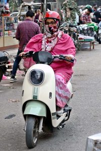 A girl confidently riding a scooty on her way to destination in the city.