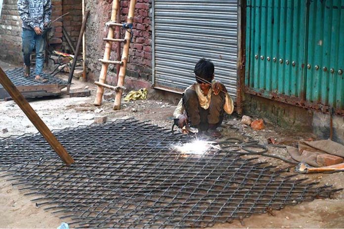 A young labourer welds an iron grill for customers outside a shop in the provincial capital